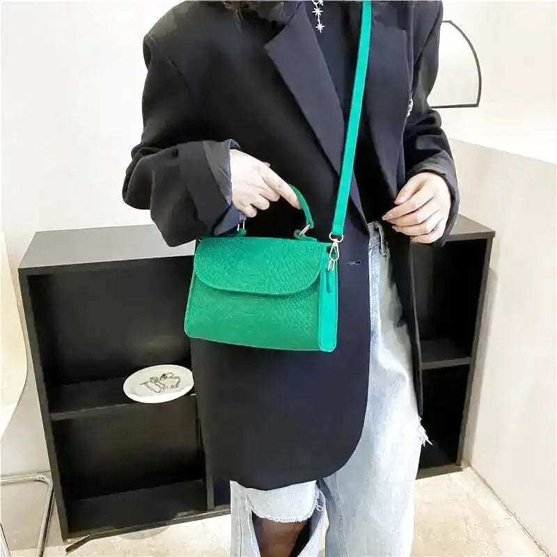 Porté en croisé sur une veste noire, le petit sac vert est tenu par son anse supérieure