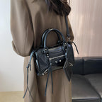 Compact et noir, le sac se porte en croisé dans le dos sur un trench beige, franges pendantes