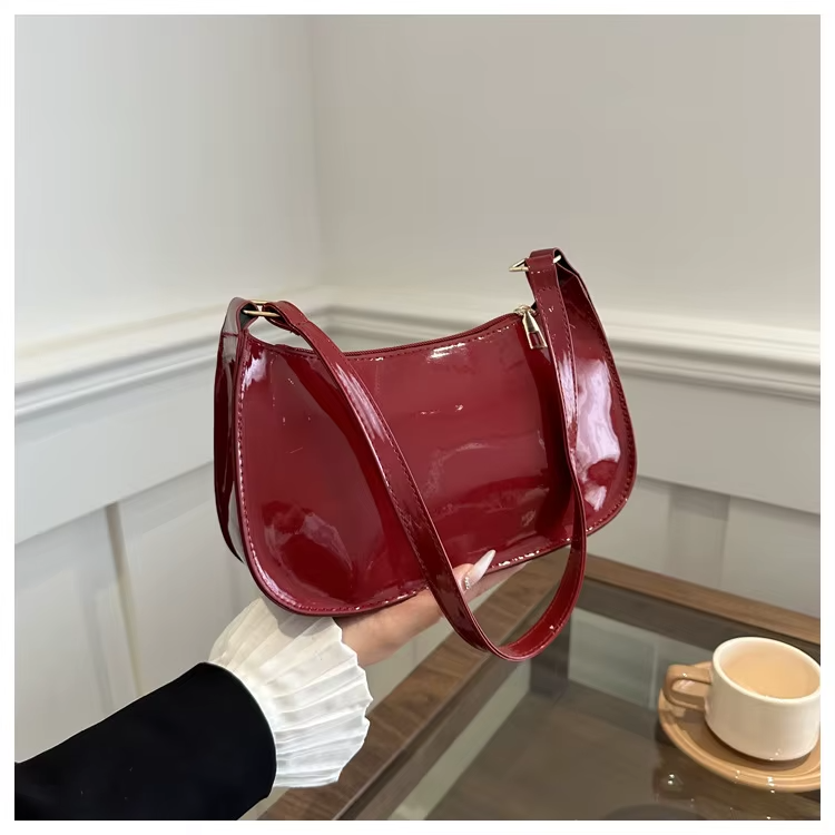 Cambrure arrondie du sac bordeaux verni tenu à la main, anse souple et surpiqûres discrètes
