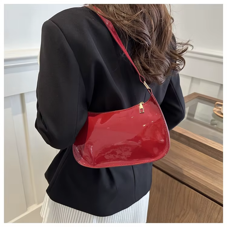 Sous le bras d'un blazer noir, le sac verni rouge bordeaux suit la ligne de la taille