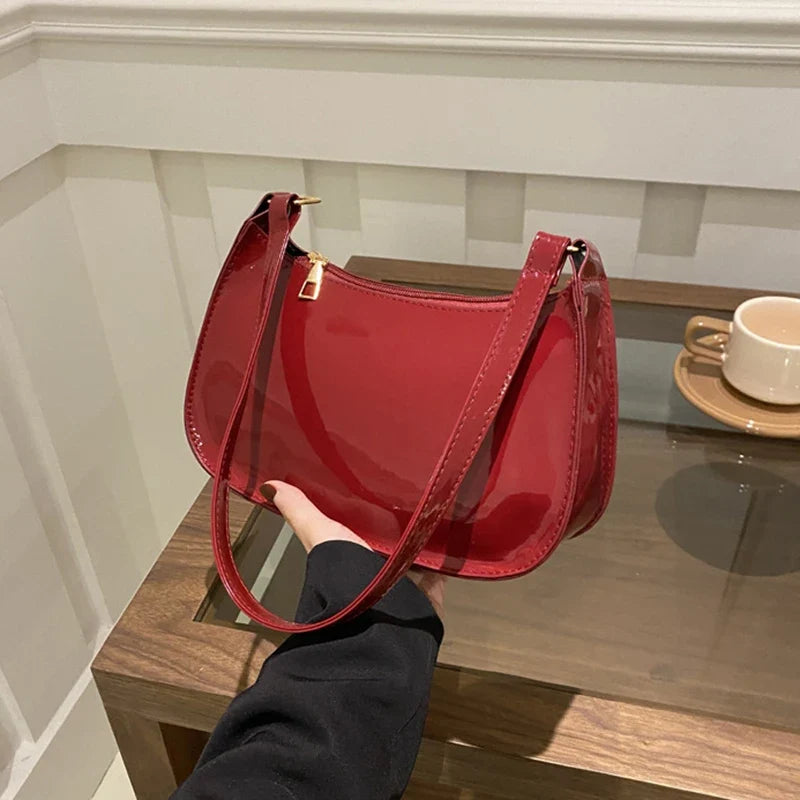 Tenu au-dessus d'une table en verre, le sac verni bordeaux reflète la lumière de la pièce