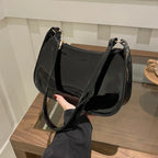 Main glissée sous l'anse, le sac verni noir laisse voir son fond arrondi et ses reflets