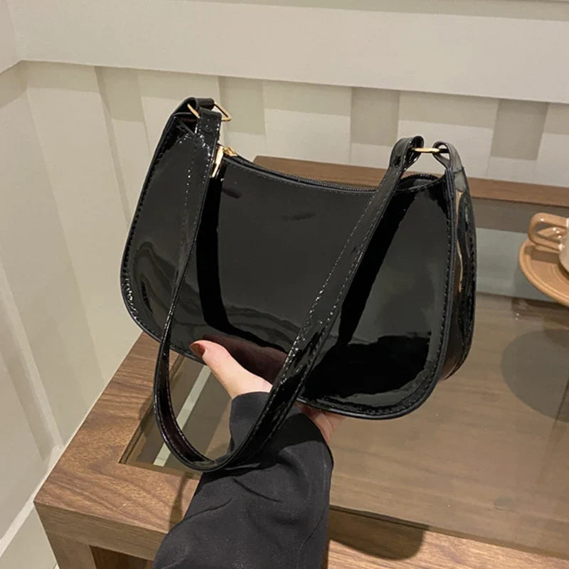 Main glissée sous l'anse, le sac verni noir laisse voir son fond arrondi et ses reflets
