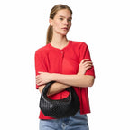 Bras croisés sur un tee-shirt rouge, une femme cale le hobo noir tressé au creux du coude