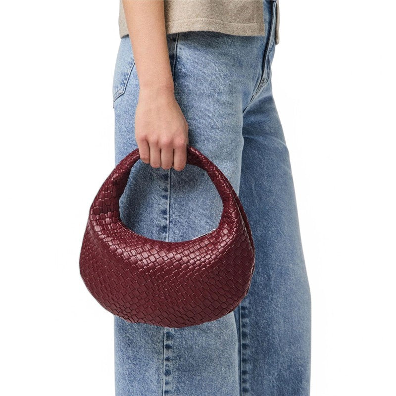 Serré dans la main le long d'un jean clair, le petit hobo tressé rouge brique tient dans la paume