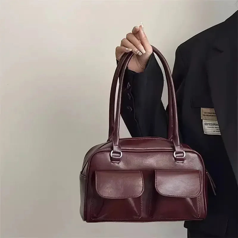 Bordeaux lustré, le sac est soulevé par ses deux anses fines devant un blazer noir