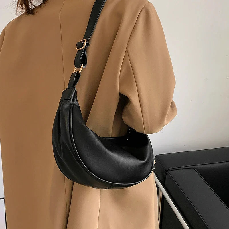 Sangle croisée sur un long manteau camel, le sac noir se cale au creux de la hanche et du dos