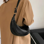 Sangle croisée sur un long manteau camel, le sac noir se cale au creux de la hanche et du dos