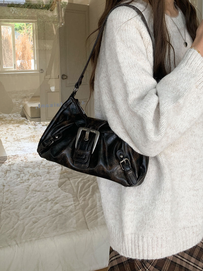 Silhouette en pull écru et jupe à carreaux, le petit sac brun suspendu à l'épaule dans une chambre