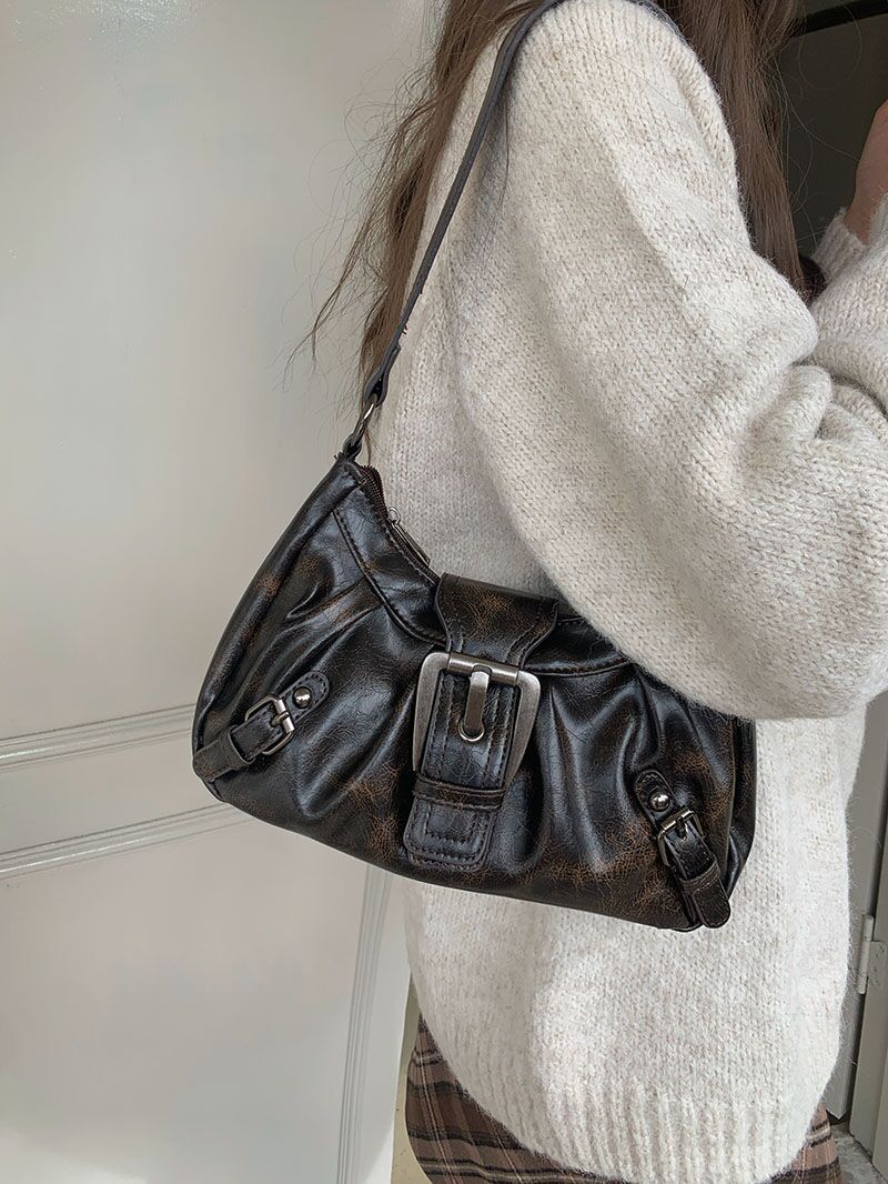 Sur un pull écru, le sac brun patiné se cale à l'épaule, grande boucle tournée vers l'avant