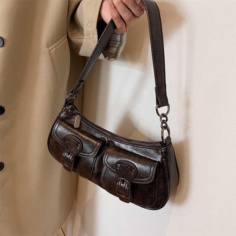 Tenu à la main devant un manteau beige, le petit sac brun foncé et sa bandoulière amovible