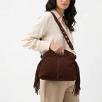Chocolat foncé, le sac à franges repose sur la hanche d'un pantalon beige, sangle en travers