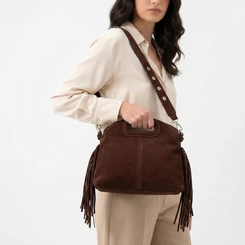 Chocolat foncé, le sac à franges repose sur la hanche d'un pantalon beige, sangle en travers