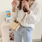 Porté en croisé sur une chemise blanche, le petit panier écru repose contre la hanche