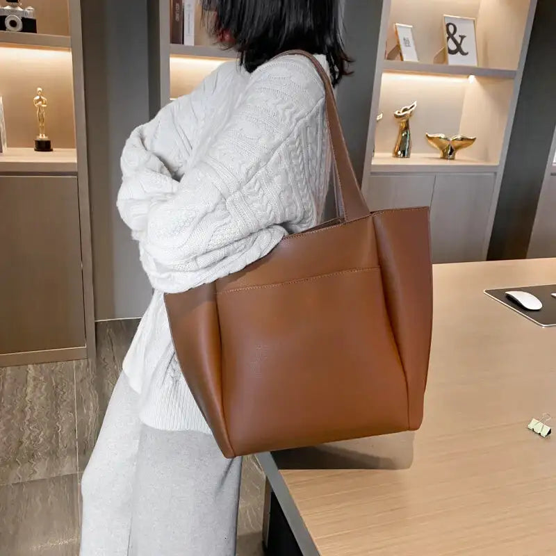 De dos, le cabas marron porté à l'épaule sur un gros pull blanc, dans un intérieur clair