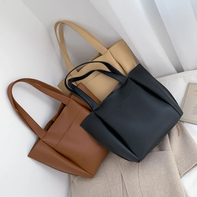 Trois coloris réunis, cabas marron, noir et beige posés sur un tissu clair, anses mêlées