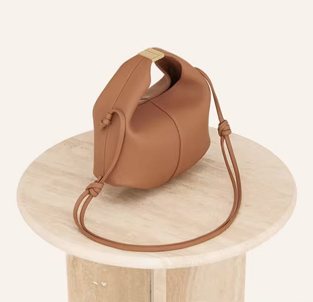 Posé sur un guéridon de pierre claire, le sac camel laisse tomber sa longue sangle nouée