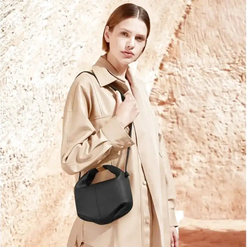 Une main sur le col de son trench beige, elle laisse pendre le mini sac noir à son cordon