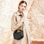 Une main sur le col de son trench beige, elle laisse pendre le mini sac noir à son cordon