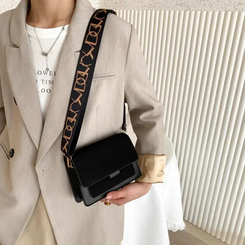 Porté en croisé sur un blazer beige, le sac noir tombe sur la hanche, sangle imprimée en travers