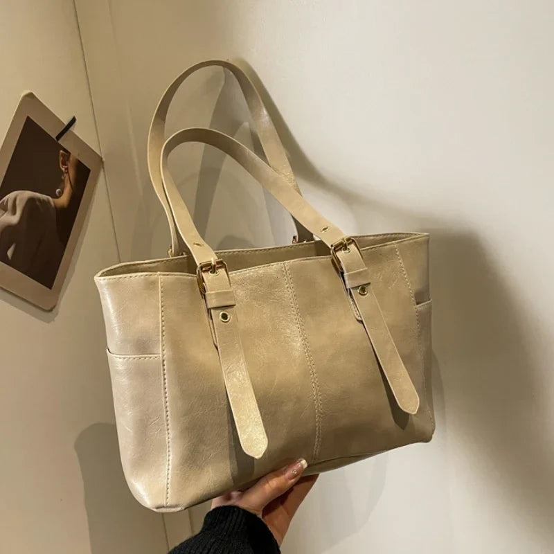 Beige doré satiné, le grand cabas est présenté anses relevées devant un mur clair et un cadre