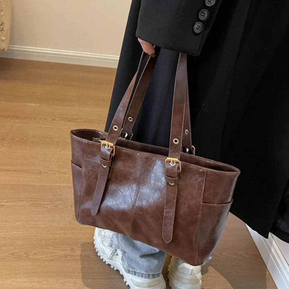 Suspendu à l'épaule d'un manteau noir, le cabas brun se détache sur un jean clair et des baskets