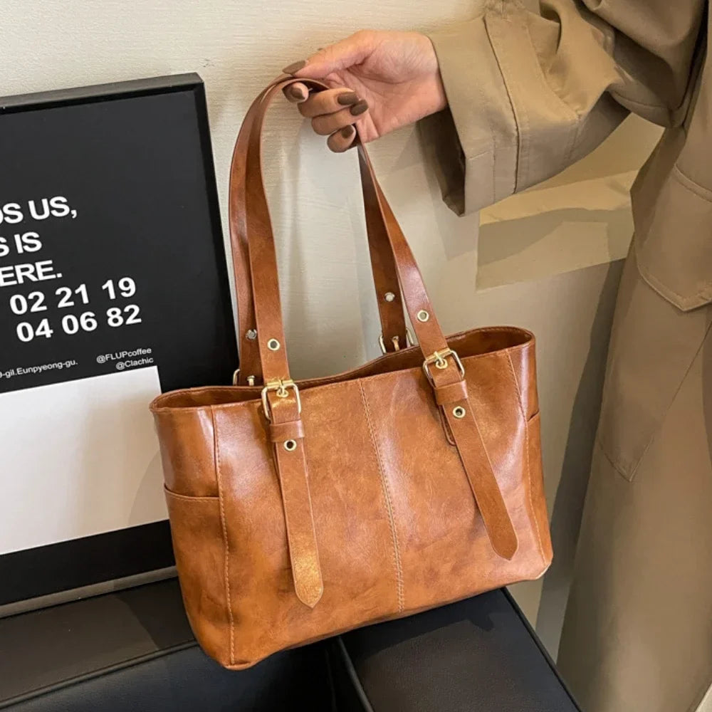 Cognac lumineux, le cabas est soulevé par ses anses, boucles dorées et cuir végan patiné visibles