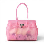 Cabas en PVC translucide rose, vu de face, fermoir cadenas argenté et contenu visible par transparence