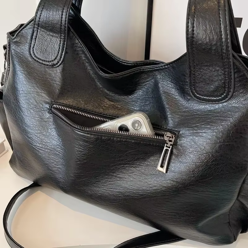 Cuir végan noir froissé en gros plan, glissière de la poche avant entrouverte sur son contenu