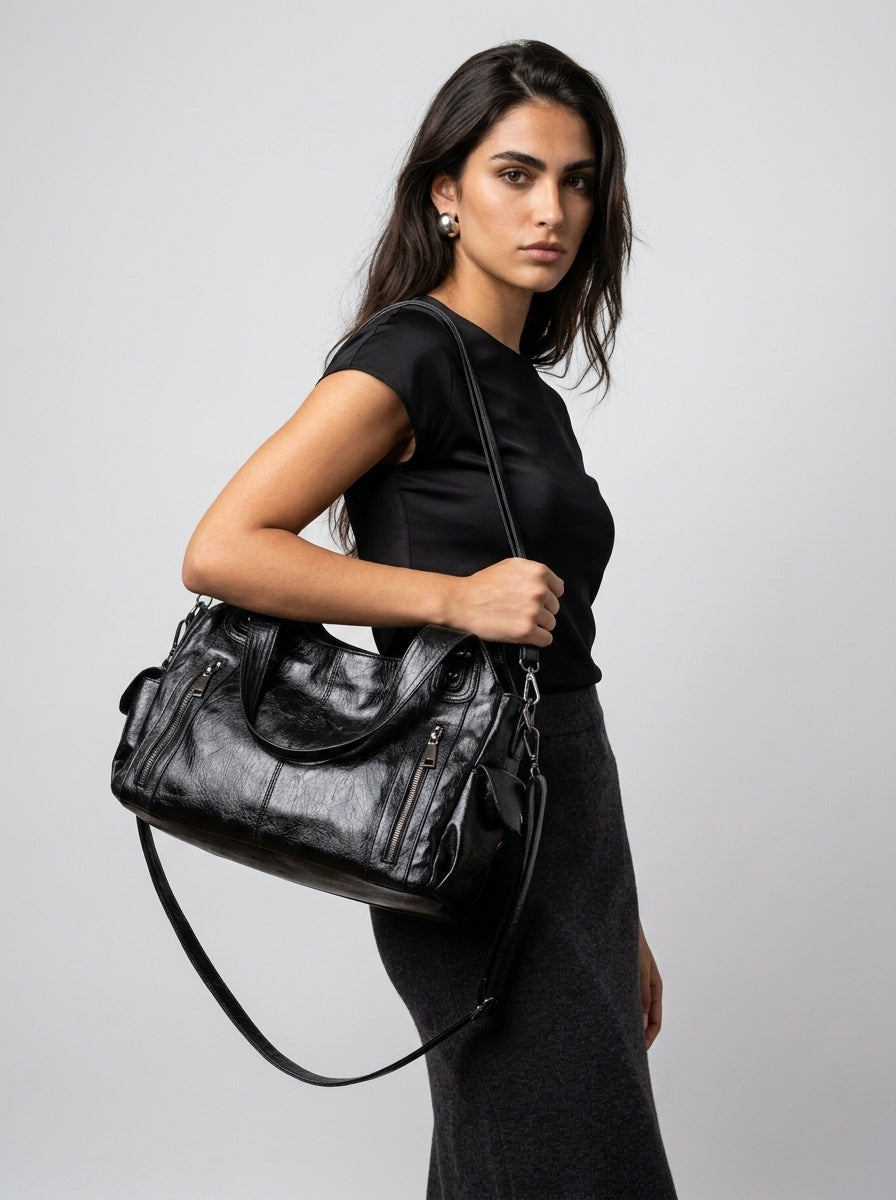 Bandoulière longue en travers du corps, le sac noir repose au creux du bras sur une robe noire