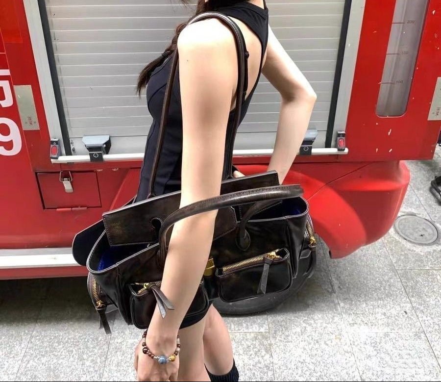 Ouvert au creux du bras, le sac brun laisse voir sa doublure bleue et ses poches intérieures