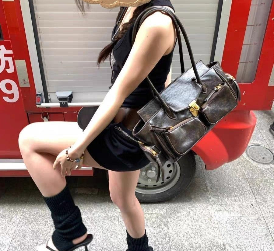 Jeune femme en robe noire, sac brun patiné porté à l'épaule devant un rideau métallique rouge