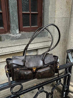 Posé sur une rampe métallique en pleine rue, le sac brun patiné montre ses poches et son clip
