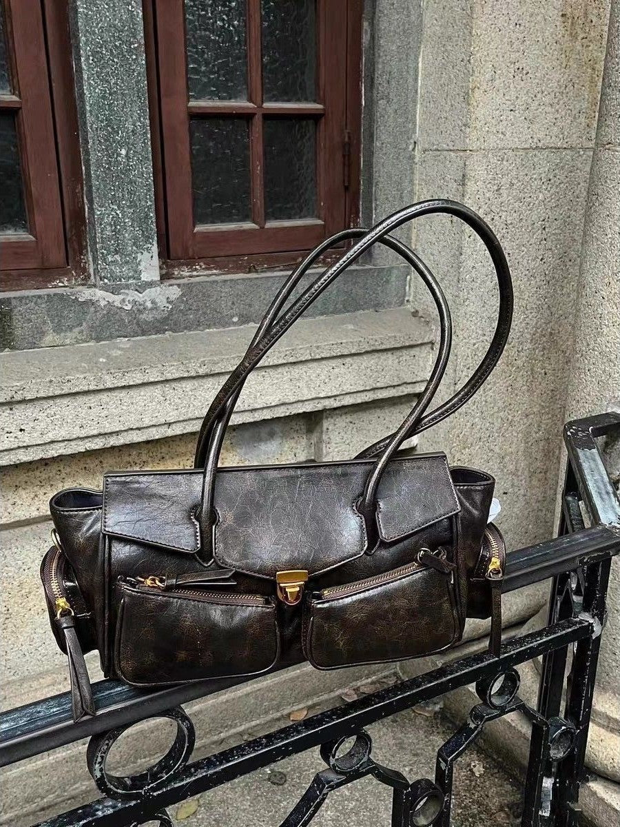 Posé sur une rampe métallique en pleine rue, le sac brun patiné montre ses poches et son clip