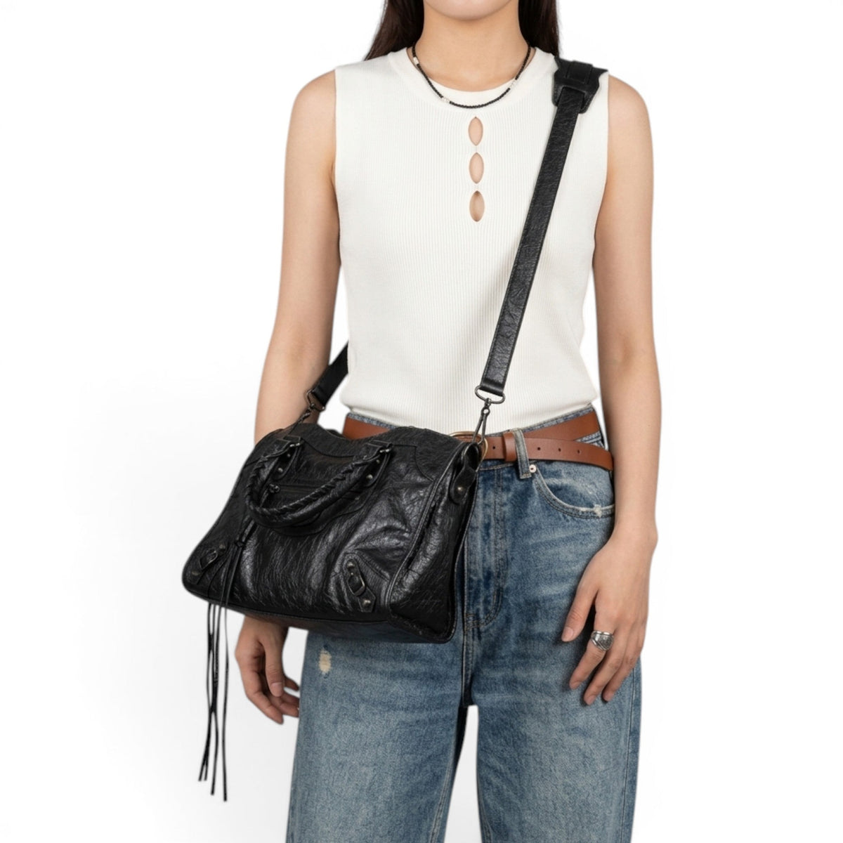 En bandoulière croisée sur la hanche, le sac noir accompagne un débardeur blanc et un jean