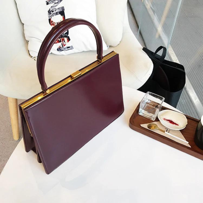 Sur un fauteuil blanc, le sac bordeaux voisine avec un plateau en bois et un verre
