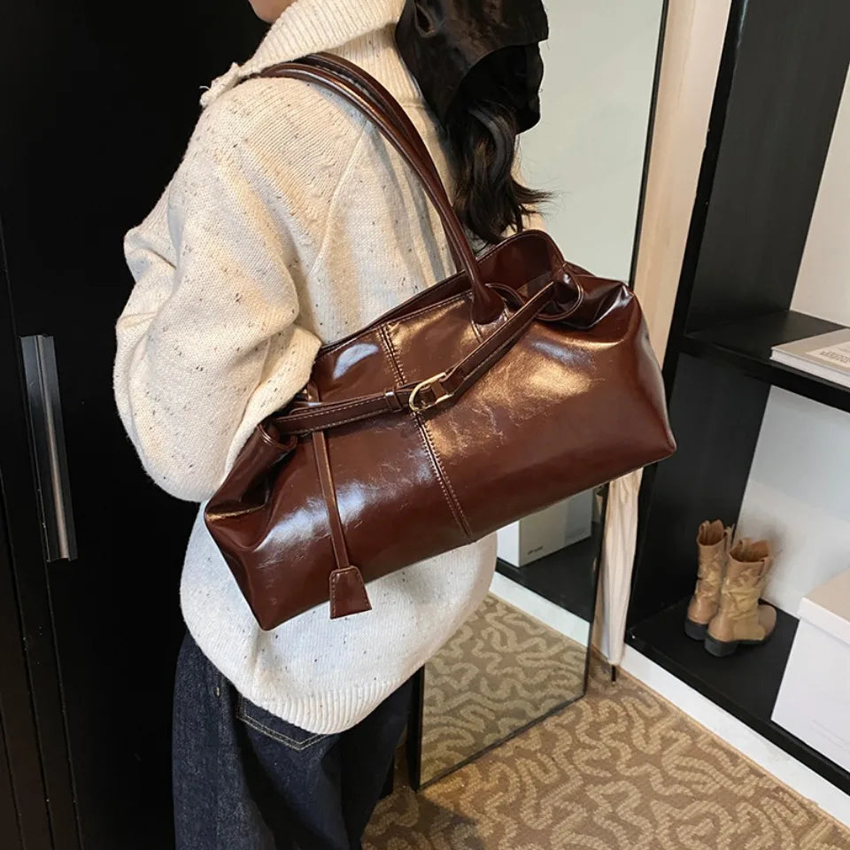 À l'épaule d'un modèle en pull crème, le sac acajou lustré s'allonge le long du buste