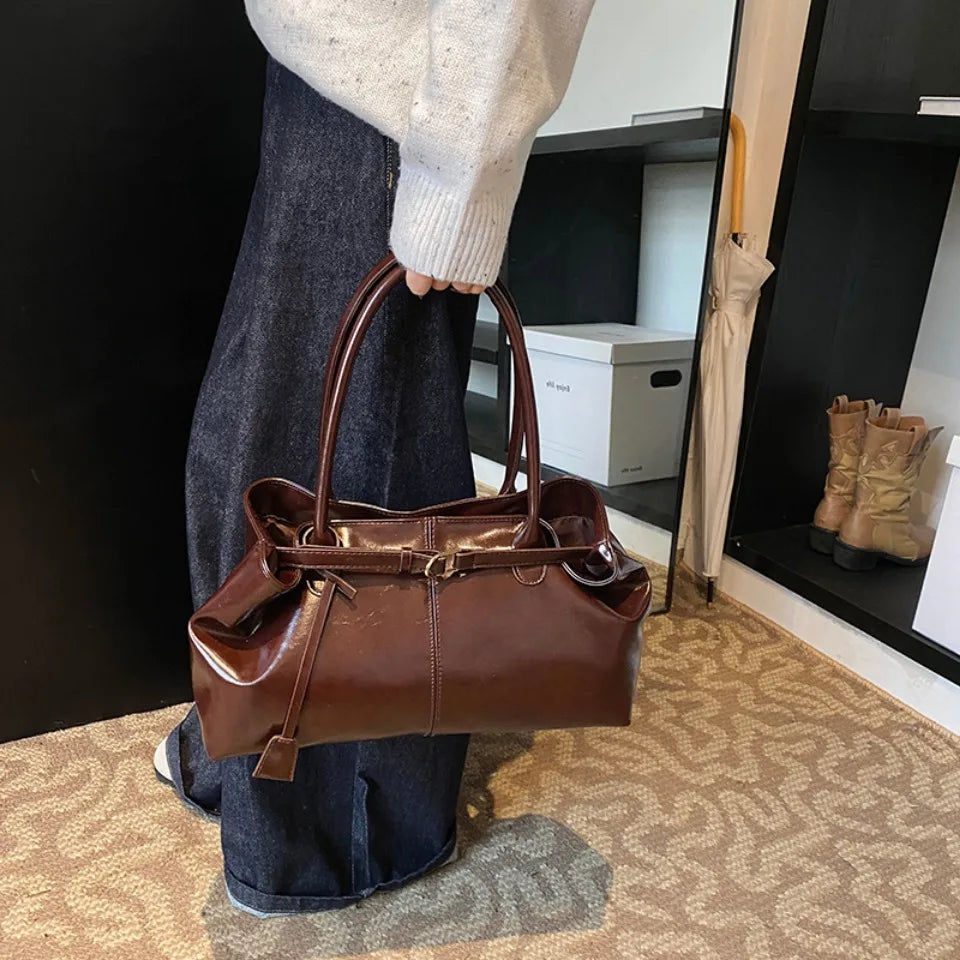 Descendant le long du jean, le sac acajou est tenu par les anses, silhouette basse et large