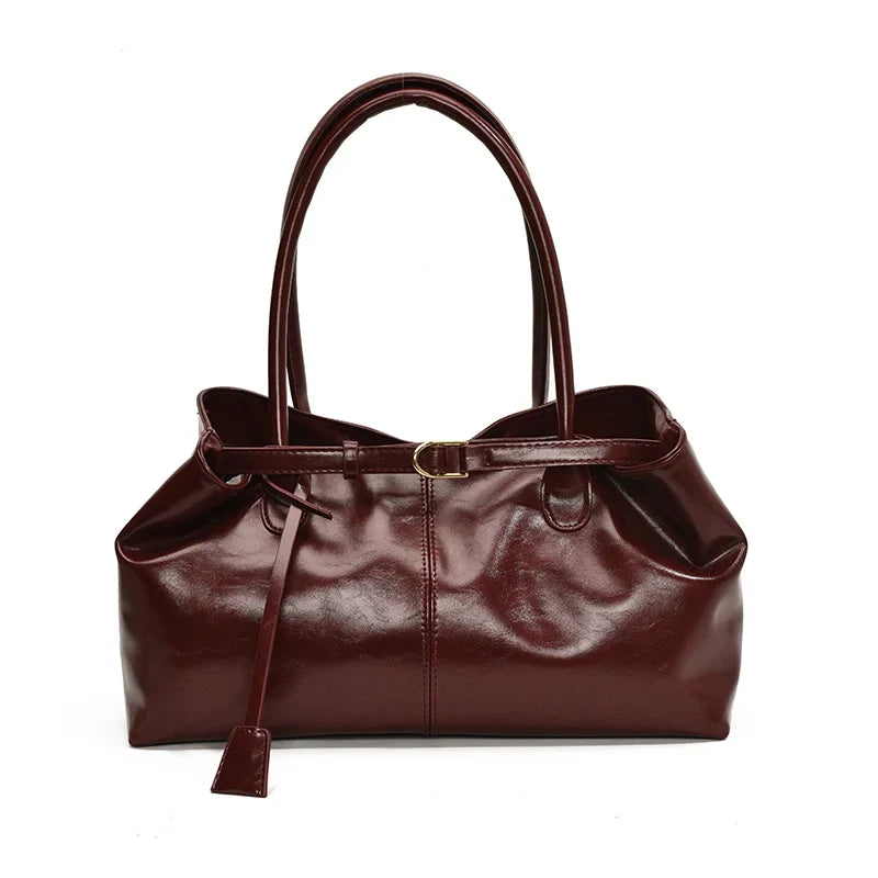 Bordeaux profond aux reflets cirés, le sac allongé est vu de face, boucle dorée au centre