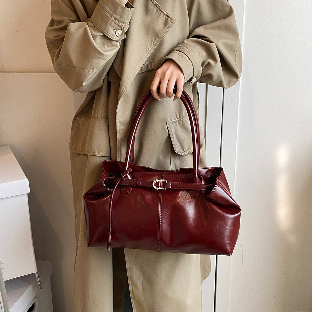 Tenu à la main devant un trench beige, le sac bordeaux montre son flanc froncé et sa ceinture