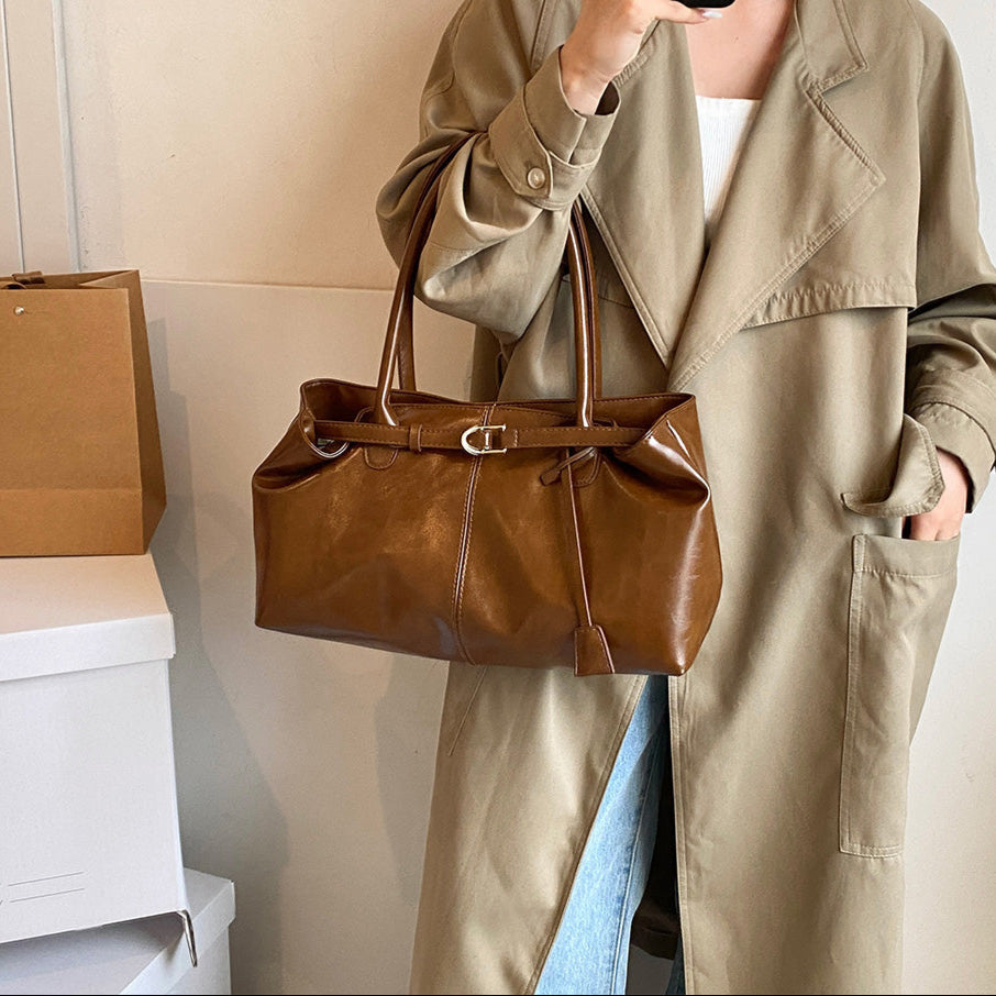 Au creux du bras d'un modèle en trench beige, le sac cognac s'étire sur toute la hanche