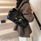 Sur une veste brun-gris dans un escalier, le long sac noir lustré se cale sous l'épaule
