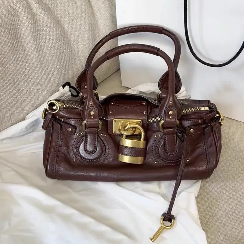 Posé sur un lit clair, le sac bordeaux foncé montre sa patine et sa clé suspendue au flanc
