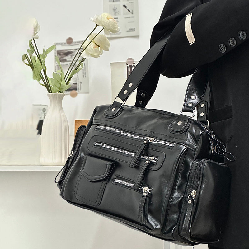 Saisi par ses anses devant un vase de fleurs, le sac noir montre ses trois poches avant