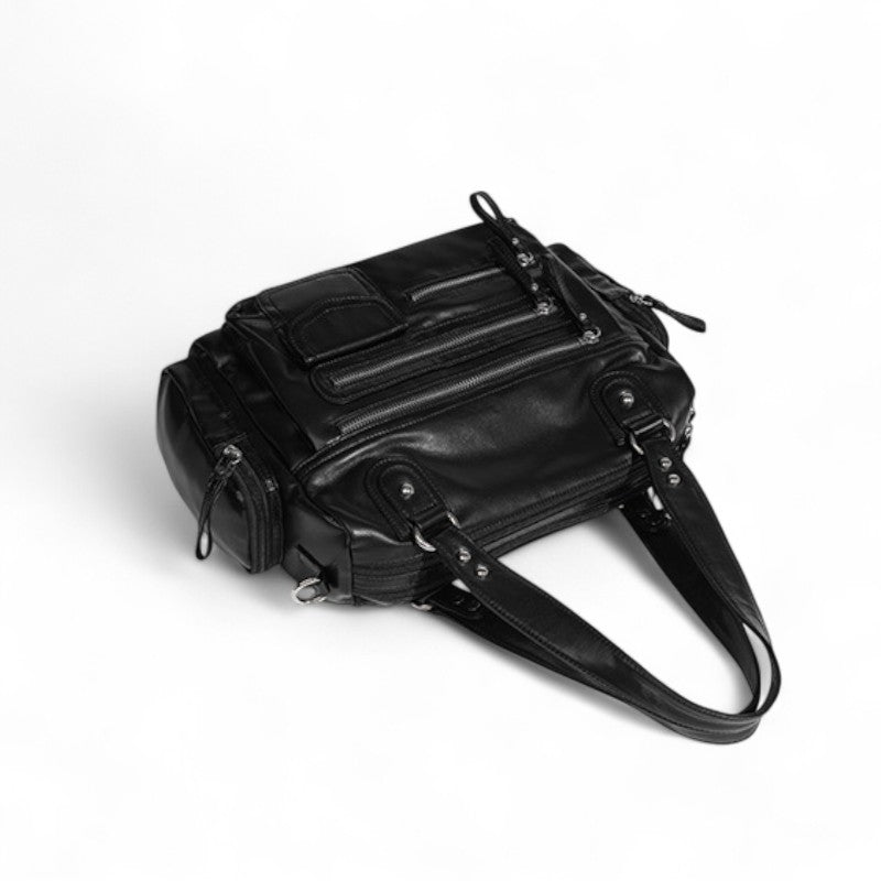 Plongée sur le sac noir couché, dessus zippé, poche plaquée et anses repliées sur le côté